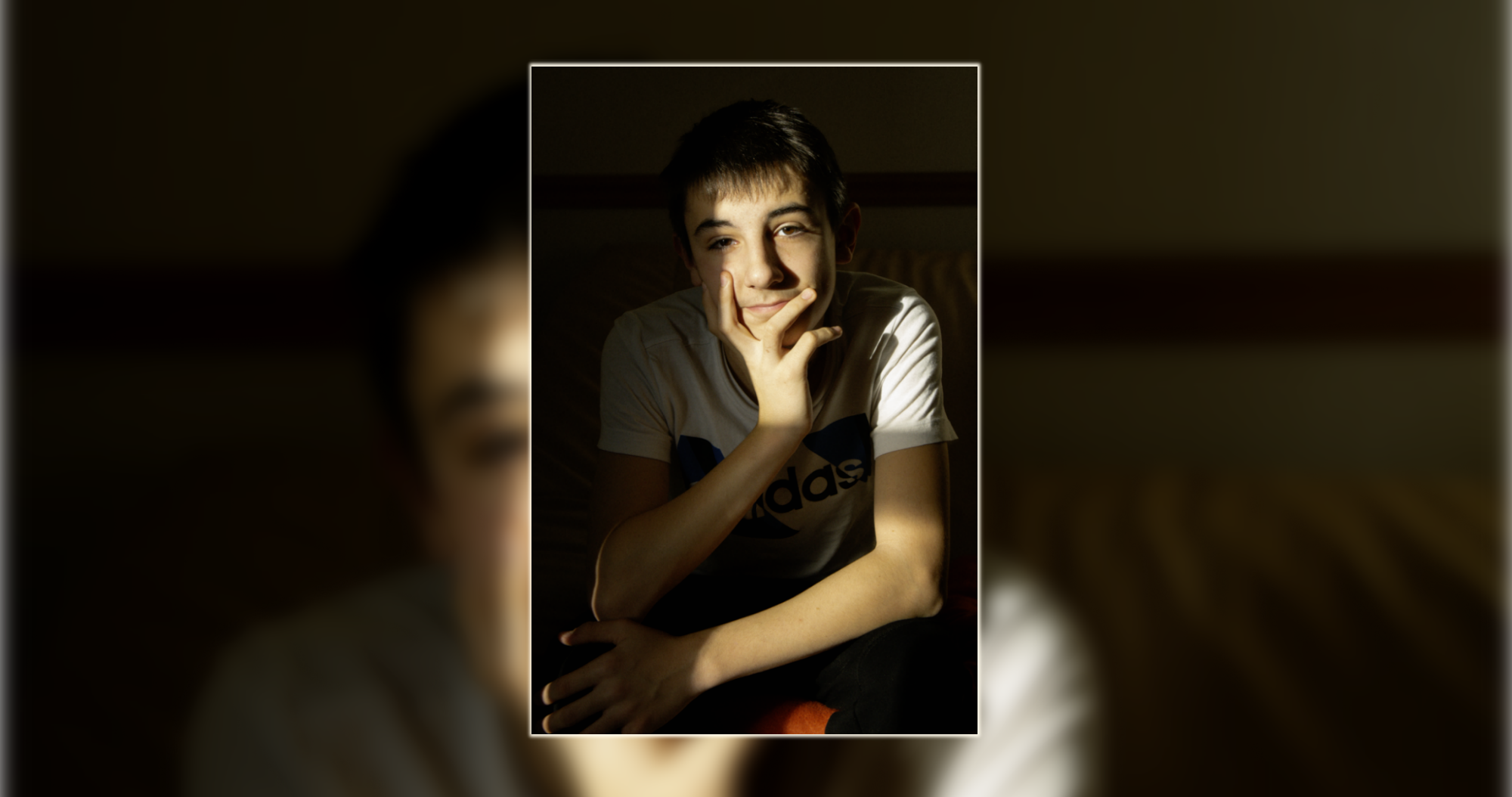 Portrait naturel intérieur – Luminéo Jeune garçon posé et souriant dans un rayon de soleil à l’intérieur – portrait naturel par Luminéo